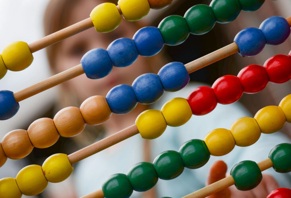 abacus-mathematics-addition-subtraction-1019470-1019470 Close-up of colorful wooden abacus with a child learning math in the background, focusing on education and early childhood development.